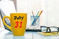 July 31st. Day 31 of month, color calendar on yellow morning coffee cup at manager workplace background. Summer time