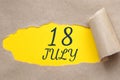 july 18. 18th day of the month, calendar date.Hole in paper with edges torn off. Yellow background is visible through
