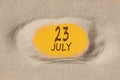 July 23. 23th day of the month, calendar date. Hole in sand. Yellow background is visible through hole