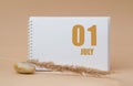 july 01. 01th day of the month, calendar date.White blank sheet of notepad, stones, dry sprig of grass, on beige