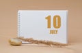 july 10. 10th day of the month, calendar date.White blank sheet of notepad, stones, dry sprig of grass, on beige