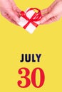 July 30th. Festive Vertical Calendar With Hands Holding White Gift Box With Red Ribbon And Calendar Date
