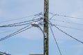 Jumble of wires connecting to the top of a wooden telephone utility pole with a street light attached to it