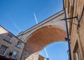 Jumbo jet aeroplane flying over railway bridge arch viaduct in blue sky with vapour trails. Low angle aircraft high in the sky Royalty Free Stock Photo