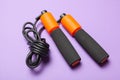 Jump rope. Fun exercises for body health. Orange rope with black cord. Violet background