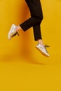 Slender female legs in black trousers and sneakers hover above the floor isolated on yellow background. Concept of Royalty Free Stock Photo
