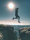 Jumping against Sun. Jumps over cliff. Man on trail through rocks/J