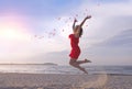 Jumping beautiful woman in red dress throwing rose petals on beach. Royalty Free Stock Photo