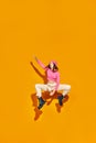 Jumping for joy in fashion. Stylish individual, young woman showcases movement and style against yellow background in