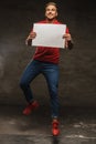 Jumping young man in jeans and red t shirt holding white sheet o Royalty Free Stock Photo