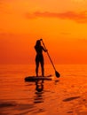 June 25, 2021. Anapa, Russia. Silhouette of woman paddle on stand up paddle board at quiet sea with sunset. Woman on Red Paddle