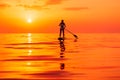 June 25, 2021. Anapa, Russia. Silhouette of woman paddle on stand up paddle board at quiet sea with sunset. Woman on Red Paddle