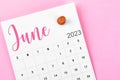 A June 2023 calendar and wooden push pin on pink colour background