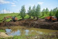 Construction equipment, a dump truck, an excavator and a tractor dig the ground for a reservoir. The village of