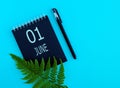 June 1th. Day 1 of month, Calendar date. Black notepad sheet, pen, fern twig, on a blue background