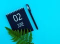 June 2th. Day 2 of month, Calendar date. Black notepad sheet, pen, fern twig, on a blue background
