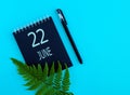 June 22th. Day 22 of month, Calendar date. Black notepad sheet, pen, fern twig, on a blue background