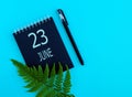 June 23th. Day 23 of month, Calendar date. Black notepad sheet, pen, fern twig, on a blue background