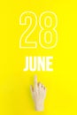 June 28th. Day 28 of month, Calendar date.Hand finger pointing at a calendar date on yellow background.Summer month, day of the