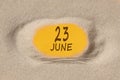 June 23. 23th day of the month, calendar date. Hole in sand. Yellow background is visible through hole