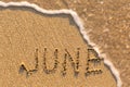 June - word drawn on the sand beach with the soft wave.