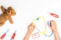 Kid hands with toy stethoscope, teddy bear and toy medicine tools on a white background. Top view. Royalty Free Stock Photo