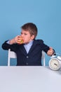 Junior in school uniform eats an apple at his desk, blue background Royalty Free Stock Photo