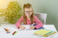 Junior schoolgirl with glasses writes something with her left hand in the notebook and sits at the table. Back to school concept. Royalty Free Stock Photo