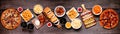 Junk food table scene, top down view over a dark wood banner background Royalty Free Stock Photo