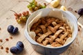 Just baked homemade apple pie in blue baking form decorated with fresh apples, grapes and brown raisins on light wooden background Royalty Free Stock Photo