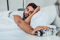 Just five more minutes. a tired young man sleeping is his bed while holding a alarm clock after getting woken up from it Royalty Free Stock Photo