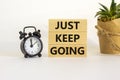 Just keep going symbol. Wooden blocks with words `Just keep going`. Beautiful white background, black alarm clock, house plant. Royalty Free Stock Photo