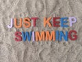 Just keep swimming written on sand at the beach