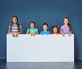 Just for the kids. Studio shot of a diverse group of kids standing behind a large blank banner against a blue background Royalty Free Stock Photo