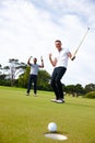Just like the pros. Low angle shot of a golf ball approaching the hole while two golfers look on. Royalty Free Stock Photo