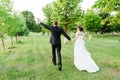 Just married couple running away happily waving their hands in a green summer garden Royalty Free Stock Photo