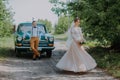 Just married wedding couple is standing near the retro vintage car in the park. Summer sunny day in forest. bride in Royalty Free Stock Photo