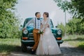 Just married wedding couple is standing near the retro vintage car in the park. Summer sunny day in forest. bride in Royalty Free Stock Photo