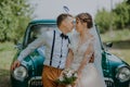 Just married wedding couple is standing near the retro vintage car in the park. Summer sunny day in forest. bride in Royalty Free Stock Photo