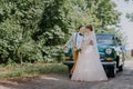 Just married wedding couple is standing near the retro vintage car in the park. Summer sunny day in forest. bride in Royalty Free Stock Photo