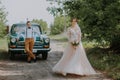 Just married wedding couple is standing near the retro vintage car in the park. Summer sunny day in forest. bride in Royalty Free Stock Photo