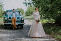 Just married wedding couple is standing near the retro vintage car in the park. Summer sunny day in forest. bride in Royalty Free Stock Photo