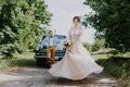 Just married wedding couple is standing near the retro vintage car in the park. Summer sunny day in forest. bride in Royalty Free Stock Photo