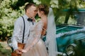 Just married wedding couple is standing near the retro vintage car in the park. Summer sunny day in forest. bride in Royalty Free Stock Photo