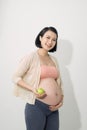 Just one apple a day. Beautiful young pregnant woman with smile and holding green apple while standing at white background Royalty Free Stock Photo