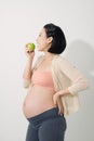 Just one apple a day. Beautiful young pregnant woman with smile and holding green apple while standing at white background Royalty Free Stock Photo