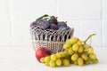 Just picked plums and grapes in wicker basket on white backdrop Royalty Free Stock Photo