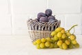 Just picked plums and grapes in wicker basket on white backdrop Royalty Free Stock Photo