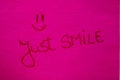 Just smile handwriting text close up isolated on pink paper with copy space. Writing text on memo post reminder