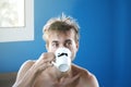 Just woke up and disheveled man drinking fresh coffee or tea from mug with painted black mustache, good weekend or weekday morning